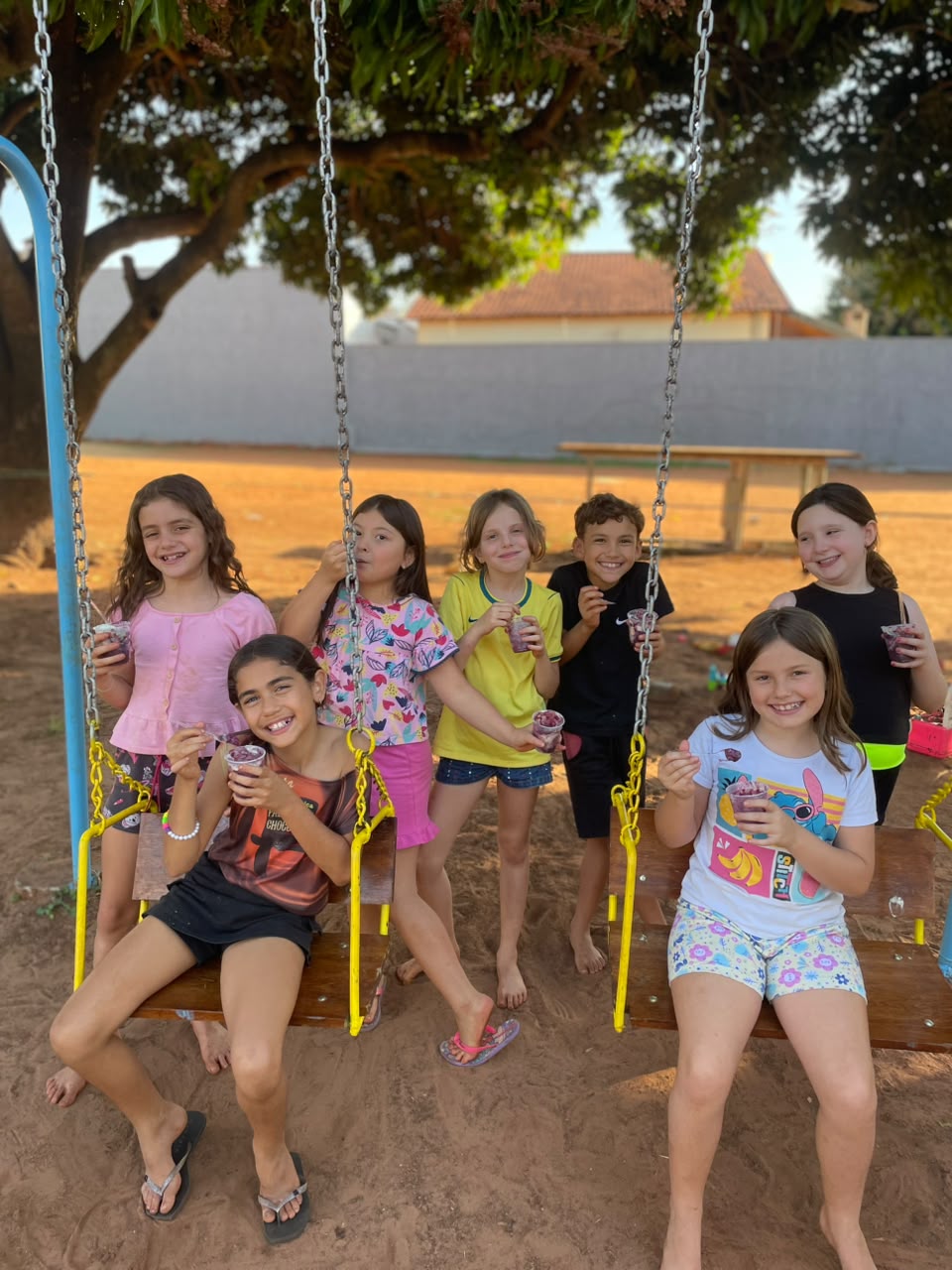 Crianças sentadas no balanço tomando açaí no fim da tarde.