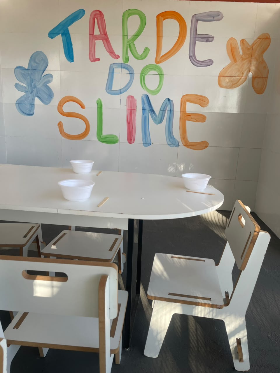 Mesa preparada para a oficina Tarde do Slime, com painel colorido pintado à mão.